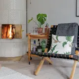 Vacker kakelugn med brinnande eld. En stol med pläd och kudde står bredvid. Kanske dags att renovera kakelugn pris?