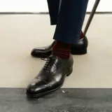 Eleganckie oksfordy, jedne z klasycznych rodzajów butów męskich, w połączeniu z bordowymi skarpetkami i granatowymi spodniami.