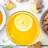 Tazza di bevanda gialla con limone, curcuma in polvere e radici, un potente antinfiammatorio naturale per intestino.