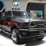 Ciemnoszary Dodge Ram 3500 z podwójnymi tylnymi kołami prezentuje się na wystawie, obok białego pickupa.