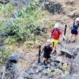 Wanderer steigen die felsige Masca Schlucht hinauf. Sie tragen Helme und Wanderstöcke.