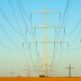 Linie energetyczne na tle błękitnego nieba. Wiele słupów wysokiego napięcia, tworzących sieć, jakby ilustrowało przelicznik MW na KW.