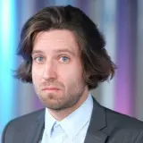 Michał Kempa w garniturze i jasnej koszuli, z burzą włosów i niebieskimi oczami.