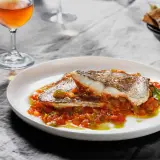 Deliciosa urta a la roteña servida en plato blanco, con guarnición de pimientos y tomate. Acompañada de copa de vino y pan.
