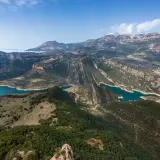 Paisaje montañoso con embalses de agua turquesa, ideal para explorar rutas Pirineos. Bosques verdes cubren las laderas y picos nevados al fondo.