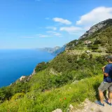 Hiker on a cliff path overlooking the blue sea and coastline.