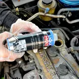 Ręce w rękawiczkach trzymają puszkę Liqui Moly Engine Flush, gotową do użycia w silniku.