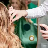 Fryzjerka utrwala fryzurę klientki, spryskując jej blond włosy lakierem. Perfekcyjny styling włosów.