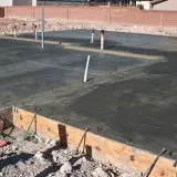 Świeżo wylany beton na płycie fundamentowej, widoczne rury i zbrojenie. Trwa izolacja pozioma fundamentów.