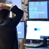 Zestresowany trader z rękami na głowie obserwuje wykresy, które mogą wskazywać na odwróconą krzywą rentowności.