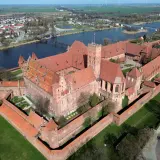 Malbork, największy zamek na świecie, z czerwonej cegły, otoczony murami obronnymi, nad rzeką Nogat.