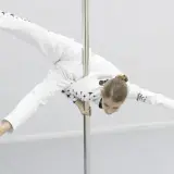 Dziewczyna w białym stroju z gwiazdami wykonuje akrobatyczną figurę na rurze. Czy pole dance to grzech? Ta młoda sportsmenka udowadnia, że to sztuka.