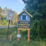 Drewniana tablica wita w Krainie Otwartych Okiennic. Obok znak Gminy Narew.