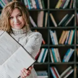 Kobieta z książką w bibliotece. Dowiedz się, jakie są zasady dystrybucji książek do bibliotek publicznych i szkolnych.