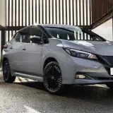 Szary Nissan Leaf stoi przed nowoczesnym budynkiem z przeszklonymi ścianami.