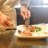 Kucharz przygotowuje danie z krewetek i warzyw, ćwicząc umiejętności do egzaminu zawodowego gastronomia.