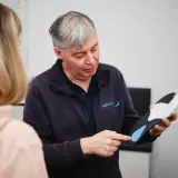 Ein Mann erklärt einer Frau, wie oft man Einlagen verschrieben bekommt, und hält eine orthopädische Einlage in der Hand.