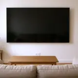 Minimalistyczny salon z dużym telewizorem zamontowanym na ścianie. Na jakiej wysokości telewizor? Idealnie, aby środek ekranu znajdował się na wysokości oczu siedzącej osoby.