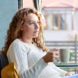Kobieta z kręconymi włosami pije kawę, zastanawiając się, jak być lepszą dziewczyną.