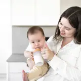 A mother smiles as she feeds her baby a bottle, a sweet moment before going back to work after maternity leave.