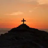 Kamienny krzyż na skalistym wzgórzu o zachodzie słońca, symbolizujący moment, kiedy umarł Jezus.