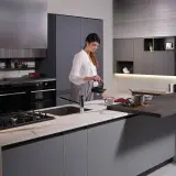 Donna prepara il tè in una moderna isola cucina fai da te con piano in marmo e bancone snack.