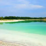 Piękne, turkusowe jezioro lazurowe odbija zielony las i błękitne niebo. Biały piasek na brzegu tworzy kontrast.
