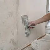 Ręka nakłada gładź na ścianę, przygotowując ją do malowania.