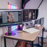 Profesjonalny monitor do obróbki zdjęć, z programem Lightroom, pokazuje zdjęcie kobiety w sukience. Obok laptop i inne monitory.