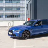 Niebieskie BMW G81 na parkingu, z nowoczesnym budynkiem w tle.