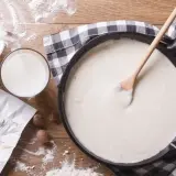 Kremowy beszamel w patelni, obok mleko, masło i gałka muszkatołowa. Idealny do zapiekanek.