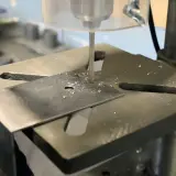 Detailaufnahme des Aufbaus einer Standbohrmaschine, die ein Metallstück bohrt.