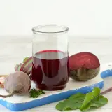 Szklanka z intensywnym, rubinowym sokiem z kiszonych buraków, obok świeże buraki i przyprawy. Zdrowie w płynie!