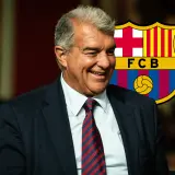 Uśmiechnięty Joan Laporta na tle herbu FC Barcelona, sugerujący udane barcelona transfery i przyszłe sukcesy klubu.
