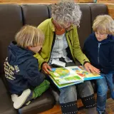 Oma und Enkel sitzen auf einer Bank und lesen gemeinsam ein buntes Bilderbuch.