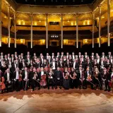 Kungliga Filharmonikerna medlemmar poserar med sina instrument i en storslagen konsertsal.
