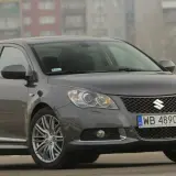Szary Suzuki Kizashi z polskimi tablicami WB 4890E zaparkowany na tle bloków mieszkalnych.