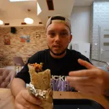 Mężczyzna z kebabem w ręku, zastanawia się, czy to bajka, czy alibaba. W tle restauracja.