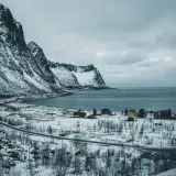 Zimowy krajobraz w Norwegii. Ośnieżone góry, spokojne morze i kilka kolorowych domków tworzą malowniczy widok podczas nocy polarnej.