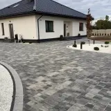 Nowoczesny dom z podjazdem z behatonu, oświetlonym stylowymi lampami.