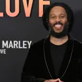 Uśmiechnięty Ziggy Marley na tle napisu "Bob Marley: One Love". Wiele dzieci Boba Marleya kontynuuje jego dziedzictwo.