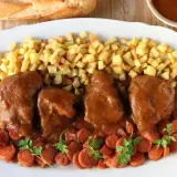 Delicioso jarrete de ternera estofado, acompañado de patatas fritas crujientes y zanahorias en rodajas.