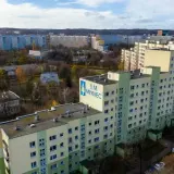 Duży blok mieszkalny S.M. Młyniec z charakterystycznym logo, otoczony innymi budynkami i drzewami jesienią.
