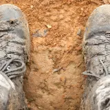 Mud-caked boots stand in dirt. The question "do boots shrink over time?" lingers as these boots look like they've seen many adventures.