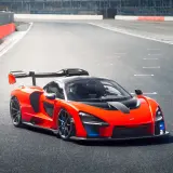 Pomarańczowy McLaren Senna z czarnym spojlerem i detalami na torze wyścigowym.
