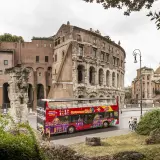 Un bus touristique rouge vif, "Citysightseeing Roma", passe devant des ruines antiques et des bâtiments romains.