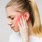 Donna con dolore al viso, area rossa indica possibile nevralgia denti o infiammazione.