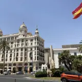 Alicante, pogoda marzec: słoneczny dzień, palmy i hiszpańska flaga nad białym budynkiem.