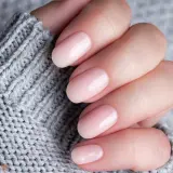 Dłoń z delikatnym, różowym manicure. Czy baza kauczukowa niszczy paznokcie? Zdjęcie sugeruje, że nie, jeśli jest stosowana prawidłowo.