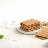Stos chrupkich wafli ryżowych na talerzyku, obok kłosów zboża i miseczki z twarożkiem. Czy wafle ryżowe są zdrowe? Tak, to świetna baza do zdrowych przekąsek.